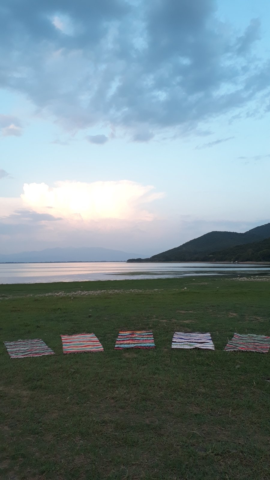 Colorful yoga mats arranged on lakeside meadow at sunset near Lake Kerkini