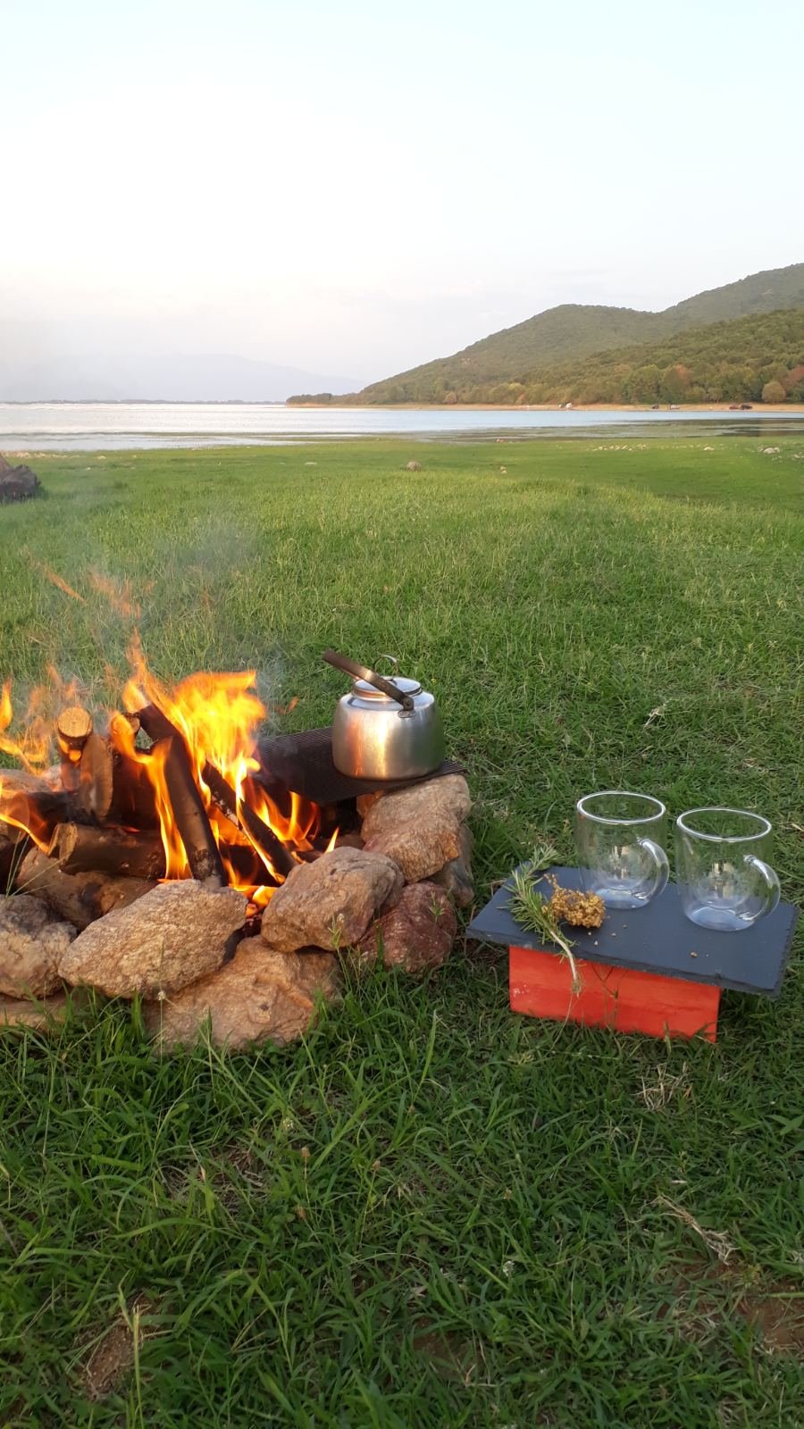 Traditional campfire with kettle and glasses by Lake Kerkini at golden hour