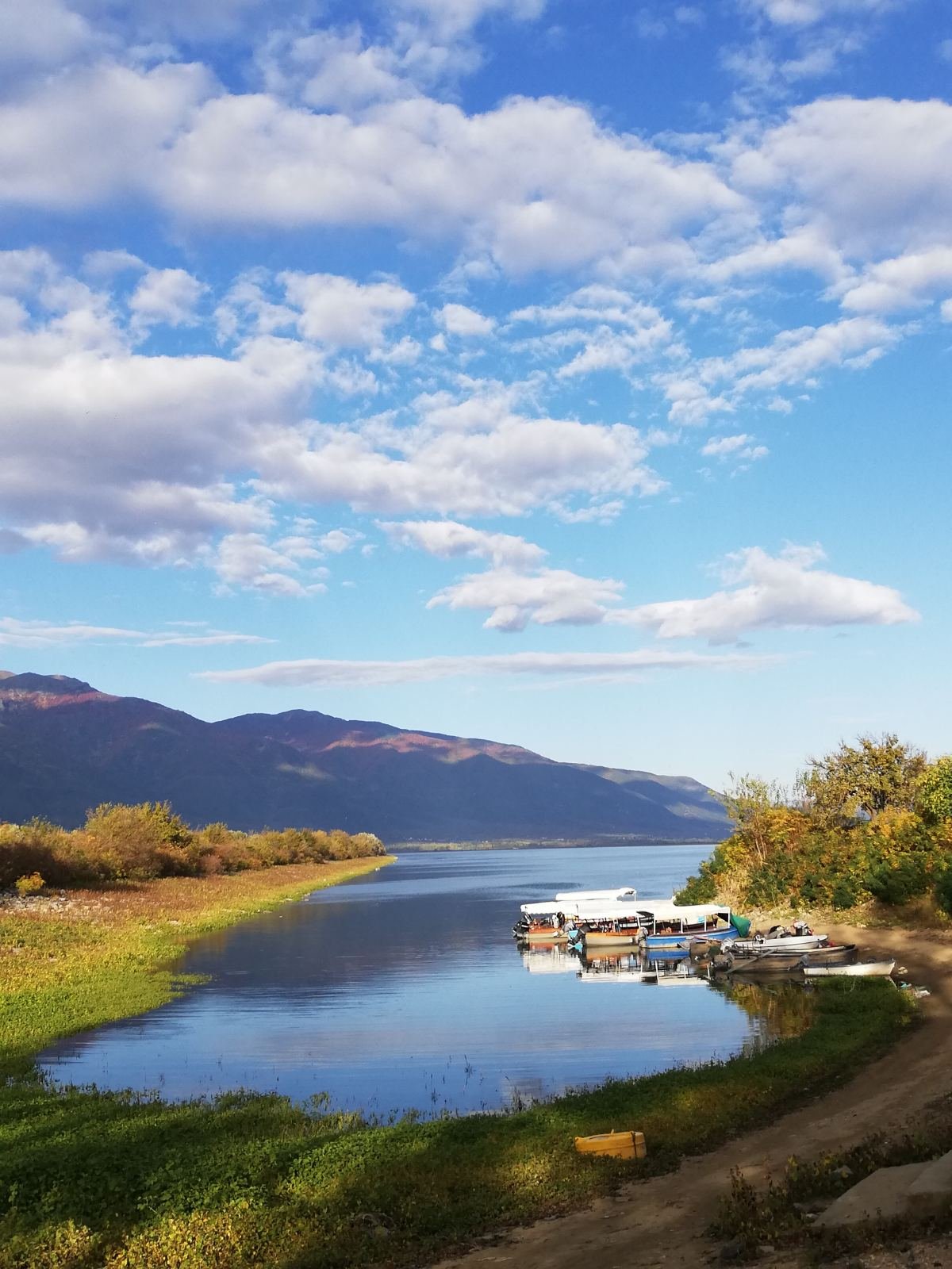 Scenic Lake Kerkini harbor with boats and dramatic mountain backdrop under blue sky